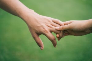 Child holding hands with adult against grass