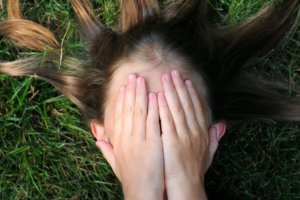 Girl covering face with hands lying on grass
