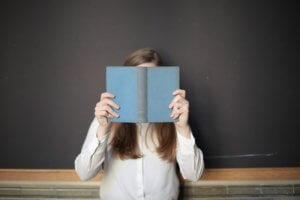 Woman in white shirt holding up book with blue cover