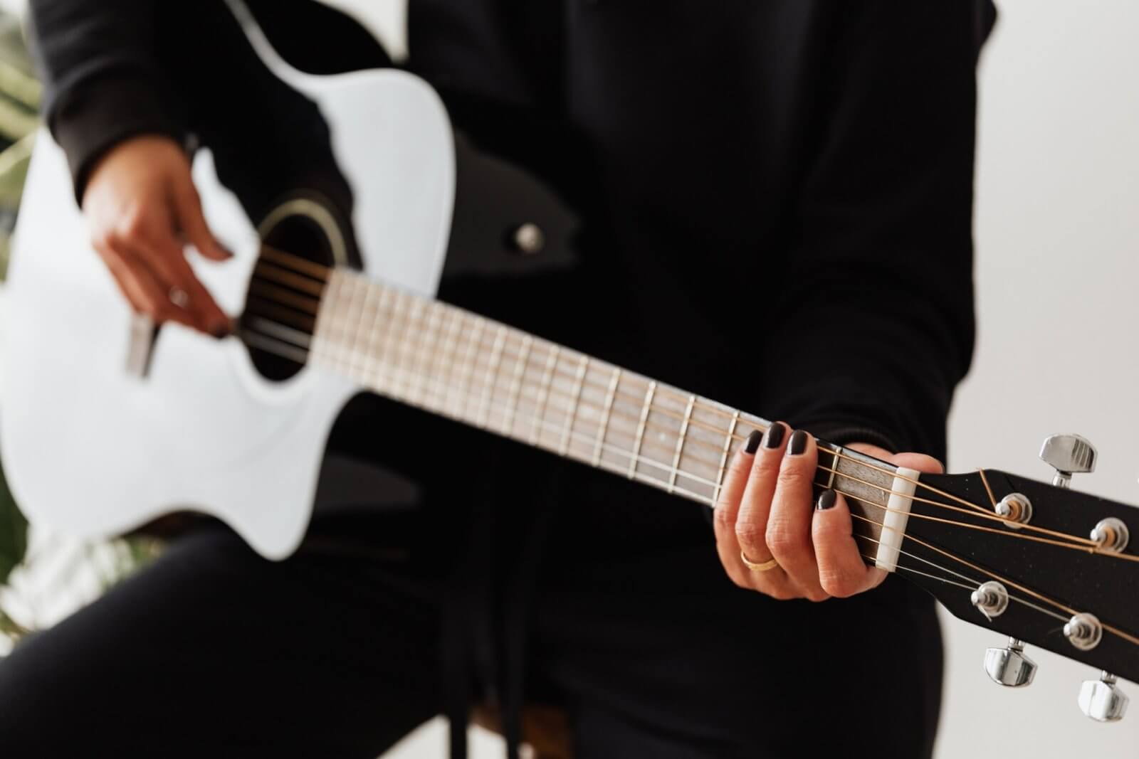 Girl dressed in black sitting on stool and playing acoustic guitar