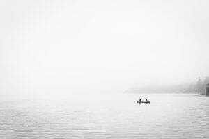 Greyscale of two people in boat on a foggy day