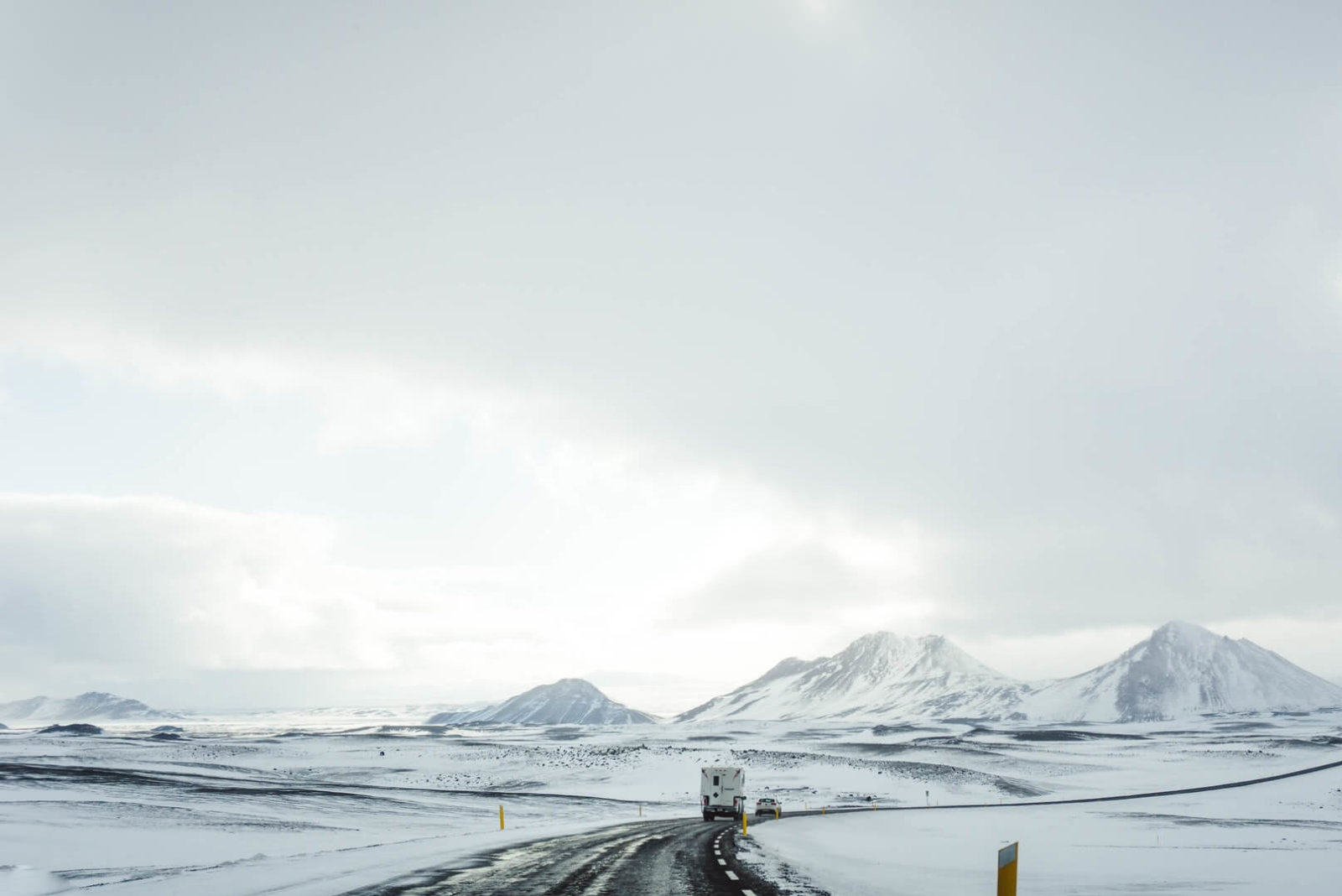 White truck and white car on snowy road towards mountains