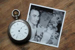 Silver pocketwatch next to old photograph of man and baby on wooden surface